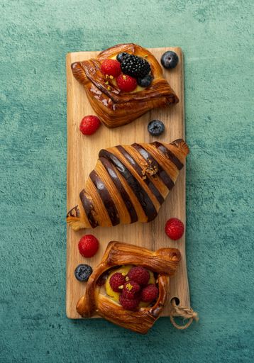 A top view of fresh pastries with berries on a wooden board over a textured green background
