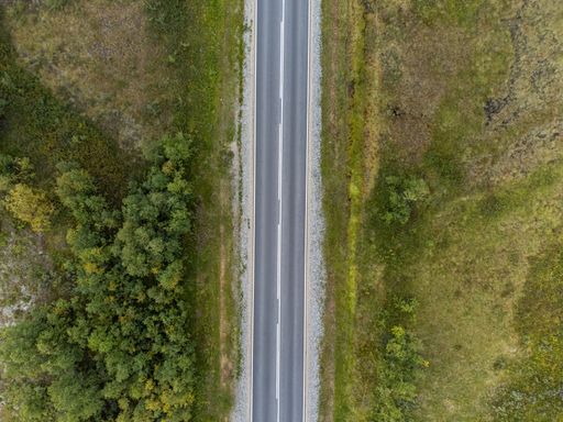 Aerial view of a straight road cutting through lush green fields and trees, showcasing nature and infrastructure harmony.