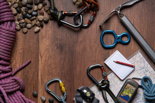Top view of wooden table with climbing equipment, rope, carabiners, ice axe, map, gps, headlamp, pocket knife and notebook