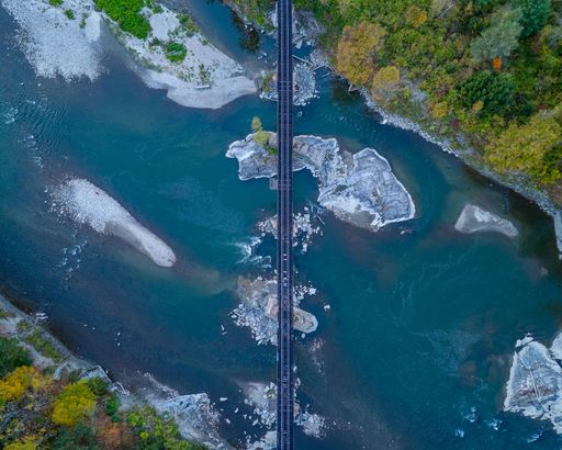 An aerial view of a bridge crossing a river with lush green foliage and rocky banks