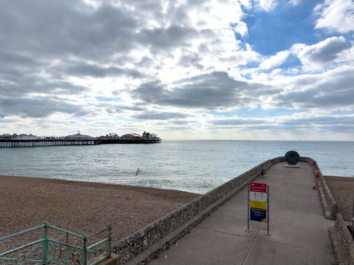 Brighton Pier and seafront under a cloudy sky, featuring a pebbled beach and a walkway, capturing a serene seaside atmosphere.