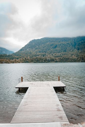 A vertical shot of a dock on a lake or a river surrounded by forest on hills on a cloudy day