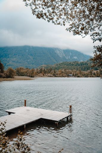 A vertical shot of a dock on a lake or a river surrounded by forests on hills on a cloudy day