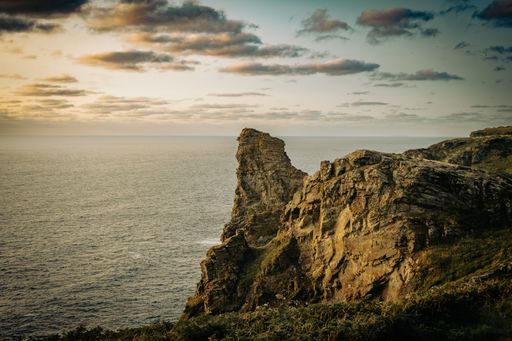A seascape with rocky seashore and a cliff under a cloudy sky
