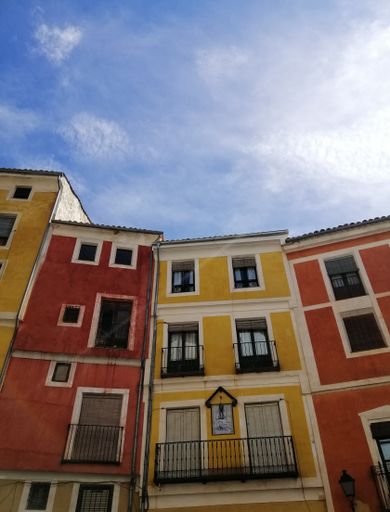 A vertical low angle shot of orange and yellow buildings in Cuenca Spain under a blue sky