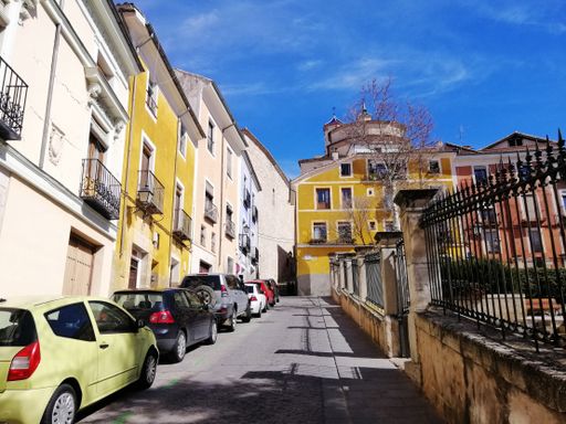 A low angle shot of a narrow pathway in between buildings and a park in Cuenca Spain
