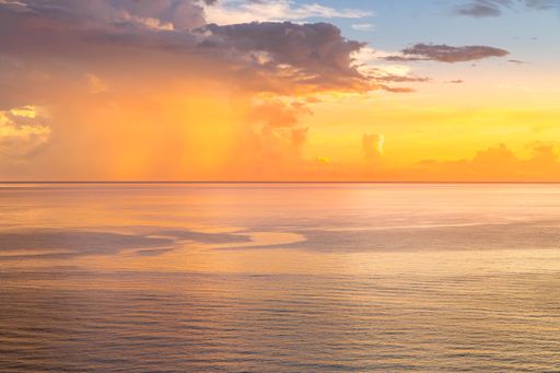 A serene ocean view at sunset with vibrant orange and yellow hues reflecting on the water. Rincon