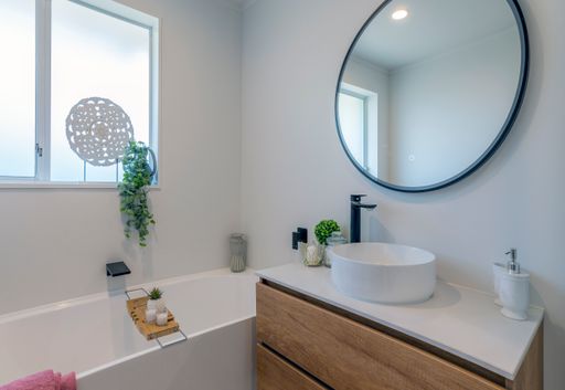 A simplistic modern bathroom with white walls, wooden drawers, and a round mirror