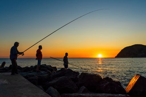 Silhoutte of three men fishing at sunset in Levanto, Cinque Terre Italy.