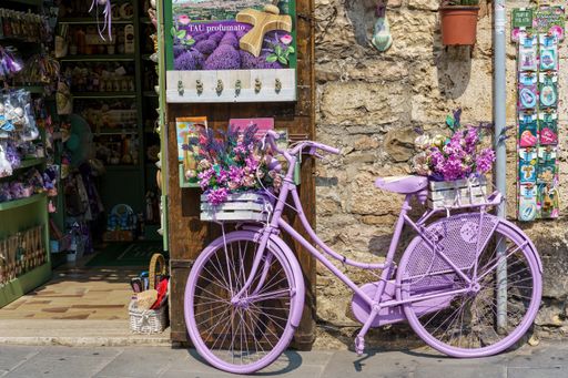 A purple bicycle decorated with flowers as a decor outside a shop on a sunny day
