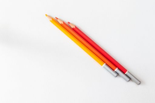 Three colorful pencils in red, orange, and yellow on a white background