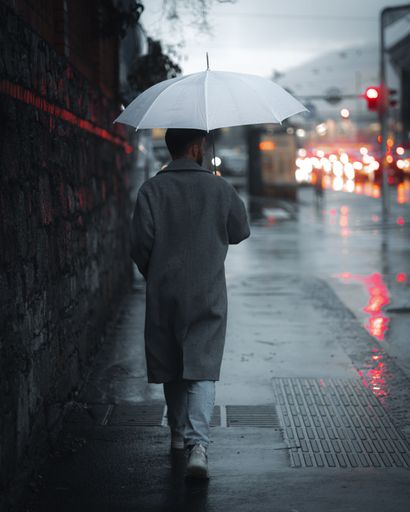 A man with a white umbrella walks on a rainy city street with blurred lights.