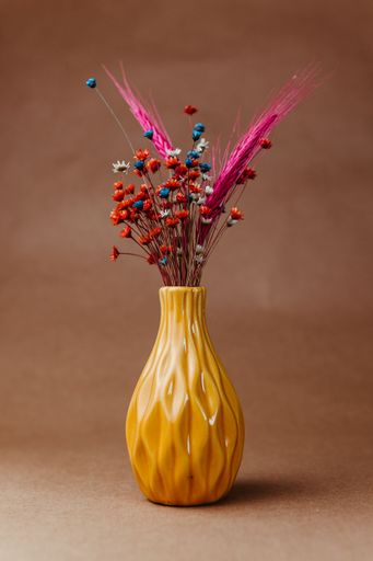 Colorful dried flowers in a yellow vase against a brown background, showcasing vibrant hues and elegant design.