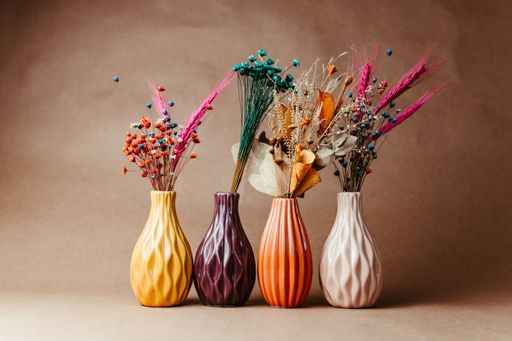 Colorful ceramic vases with dried flowers arranged on a neutral background, showcasing vibrant home decor.
