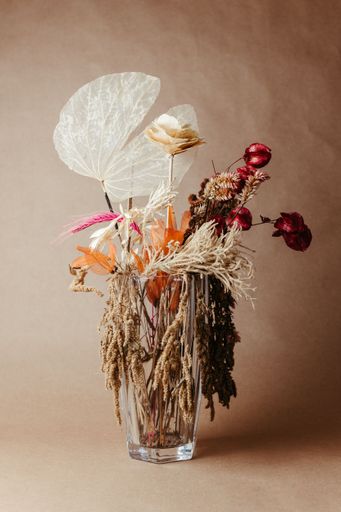 Aesthetic arrangement of dried flowers in a clear vase against a brown background, showcasing natural textures and earthy tones.