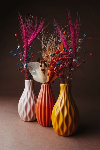Elegant ceramic vases in pink, orange, and yellow with vibrant dried flowers against a brown background.