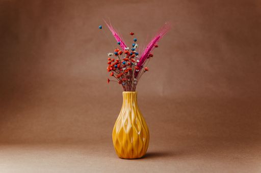 Colorful dried flowers in a yellow vase against a brown background, showcasing a simple yet elegant decor piece.