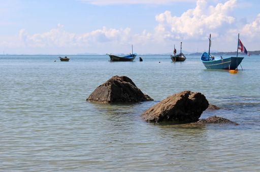 Rocks in a bay by the shore with small traditional Asian wooden fishing boats moored in the background, southeast Asia