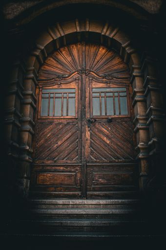 A vintage wooden door with intricate carvings and an arched frame, set in a dimly lit stone entrance.