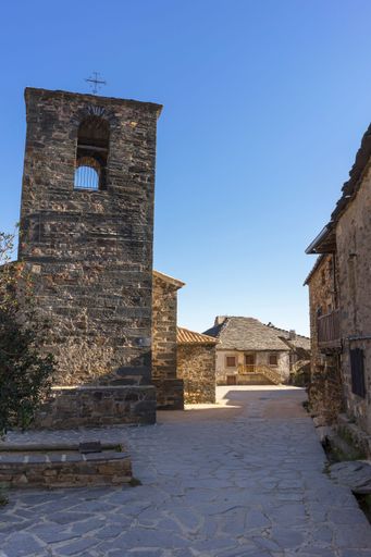 A stone bell tower rises in a charming village featuring cobblestone streets and traditional architecture beneath a clear sky.