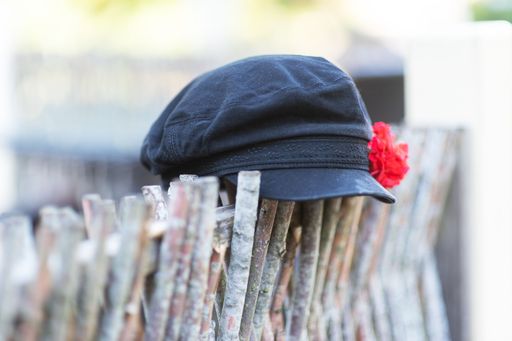 A closeup shot of a black women beret with red flower, hanging on a wooden fence on a sunny day, with blurred background