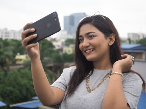 Young female happily taking selfies while Standing in terrace Medium shot of a pretty Indian girl posing while clicking pictures using a smartphone