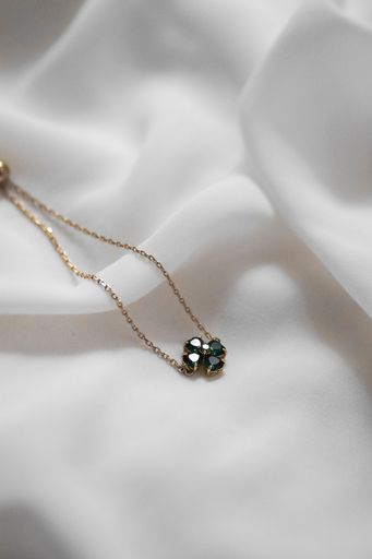 Elegant gold necklace with a green gemstone pendant on soft white fabric background.