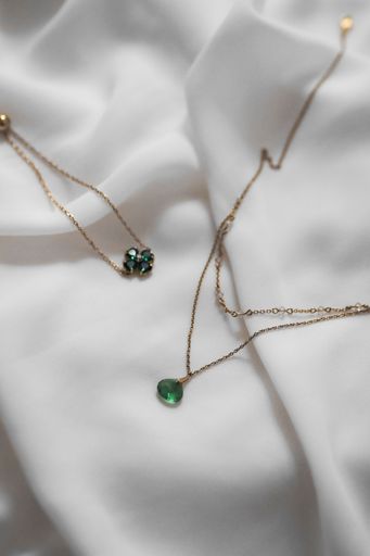 An elegant gold necklaces with green gemstone on white fabric background, showcasing luxury and style.
