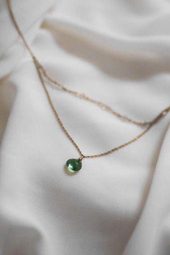 Elegant gold necklace with green gemstone on white fabric background, showcasing luxury and style.