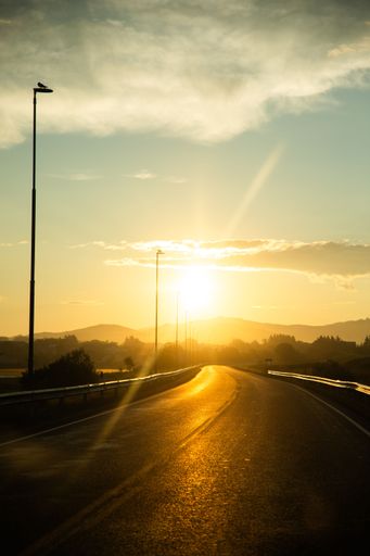 A golden sunset over a winding road with streetlights and mountains in the background
