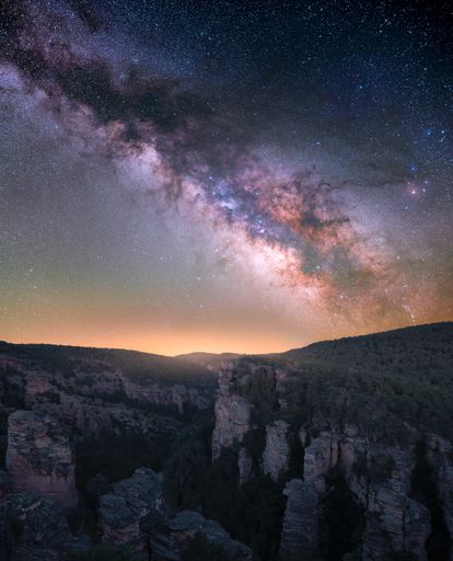 A vertical stunning photo of the milky way core above cliffs