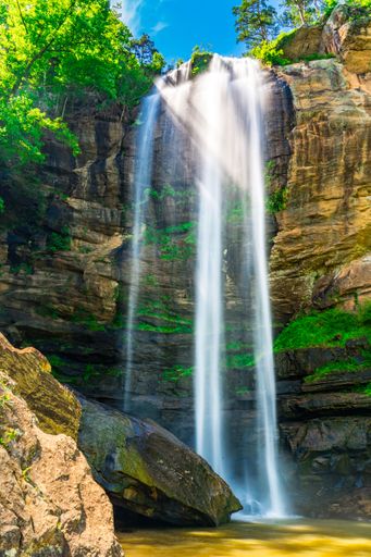 A stunning waterfall cascading over a rocky cliff surrounded by lush greenery under a bright blue sky.