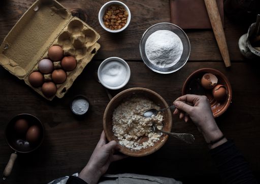 A cook baking pastry in the kitchen with different ingredients on the table