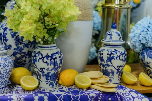 Elegant still life with blue and white porcelain vases, yellow flowers, lemons, and wooden utensils on a patterned tablecloth.