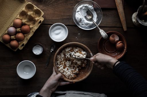 A cook baking pastry in the kitchen with different ingredients on the table