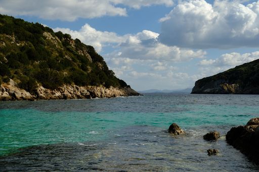 Scenic coastal view with turquoise waters and rocky cliffs under a partly cloudy sky, capturing the essence of a tranquil seaside landscape.