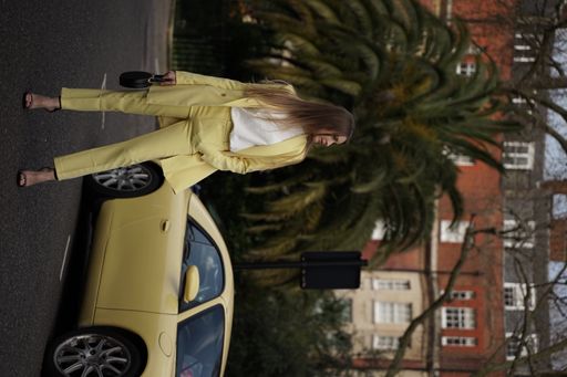 A Caucasian female in a white and yellow outfit posing for the camera outdoors in front of the car
