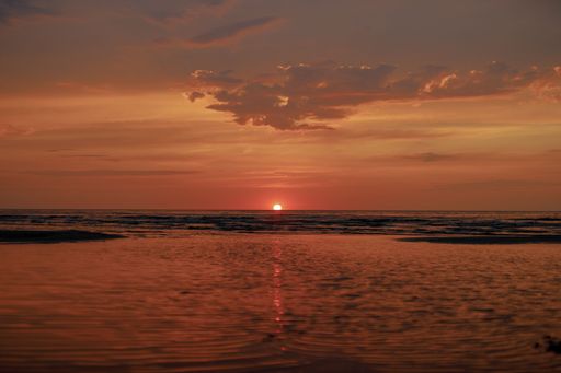 A serene sunset over a calm ocean, with vibrant orange and red hues reflecting on the water's surface.