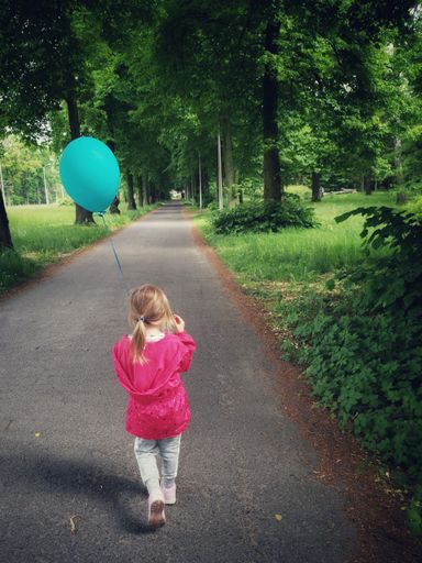A vertical shot of a blonde girl walking in a park holding a blue balloon