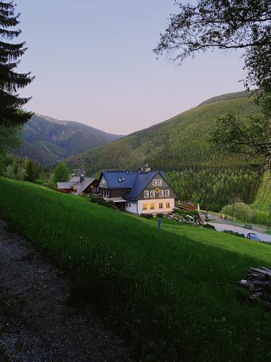 Charming countryside house nestled in lush green mountains under a clear evening sky, showcasing serene rural landscape.