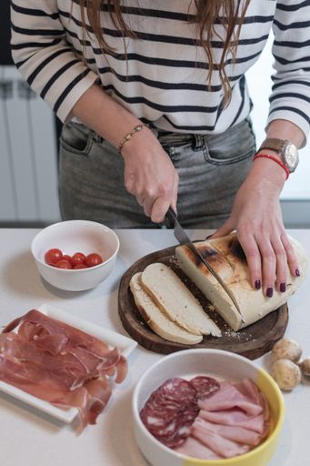 A closeup shot of female hands cutting bread on a wooden board with other ingredients
