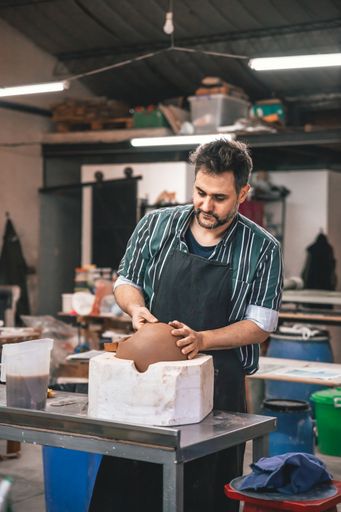 An adult Hispanic man making a clay pot on a table in a workshop