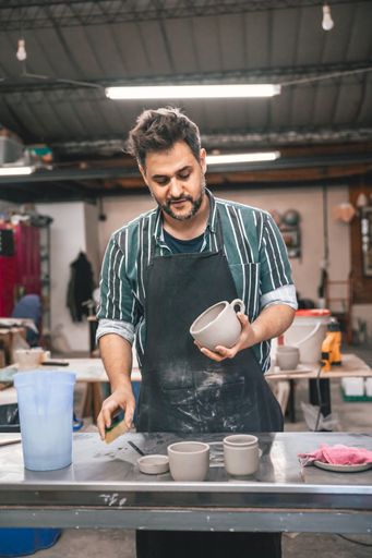An adult Hispanic man polishing a clay pot above a table in a workshop