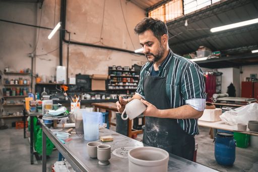 An adult Hispanic man polishing a clay pot above a table in a workshop