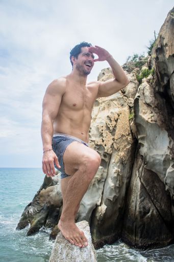 A vertical shot of an athletic Hispanic man happily looking at a distance during a holiday at a beach