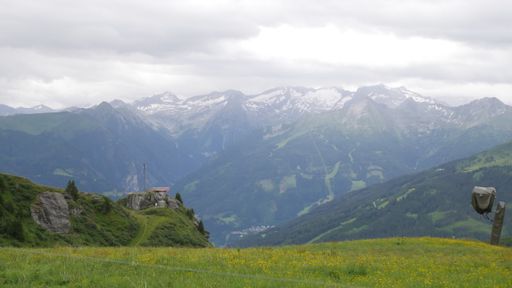 a green field and a snowy mountain range under the clouds