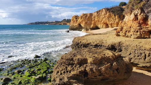 Scenic view of Algarve coastline with rocky cliffs and ocean waves under a partly cloudy sky.