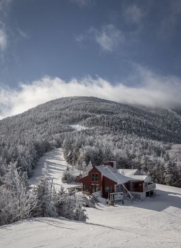 A snow-covered ski lodge at Sugarbush ski resort in Vermont nestled in a winter landscape with a clear blue sky and forested mountain backdrop.