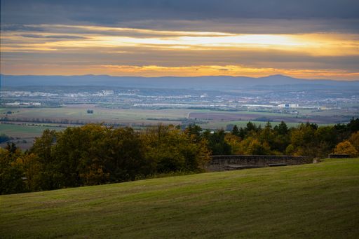 Scenic view of a sprawling landscape with a sunset sky over a distant city and rolling hills.