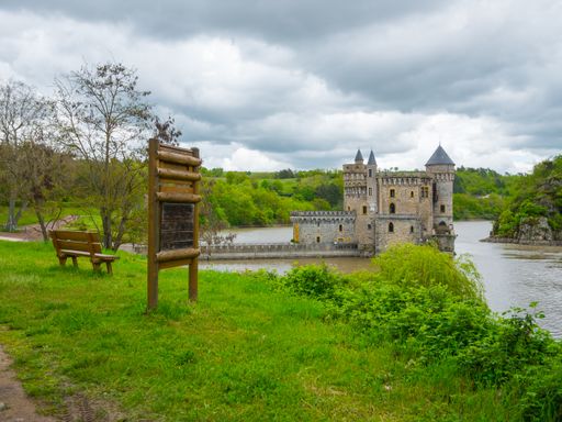 A castle Chateau de la Roche on Loire river in france with dense forest, bench and signboard